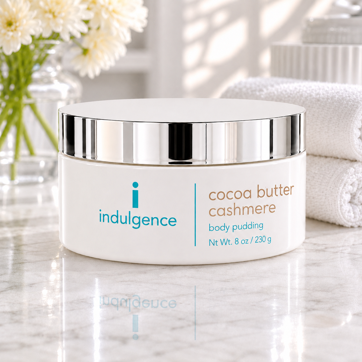 Indulgence cocoa butter cashmere body pudding jar on a marble surface with flowers and towel in the background