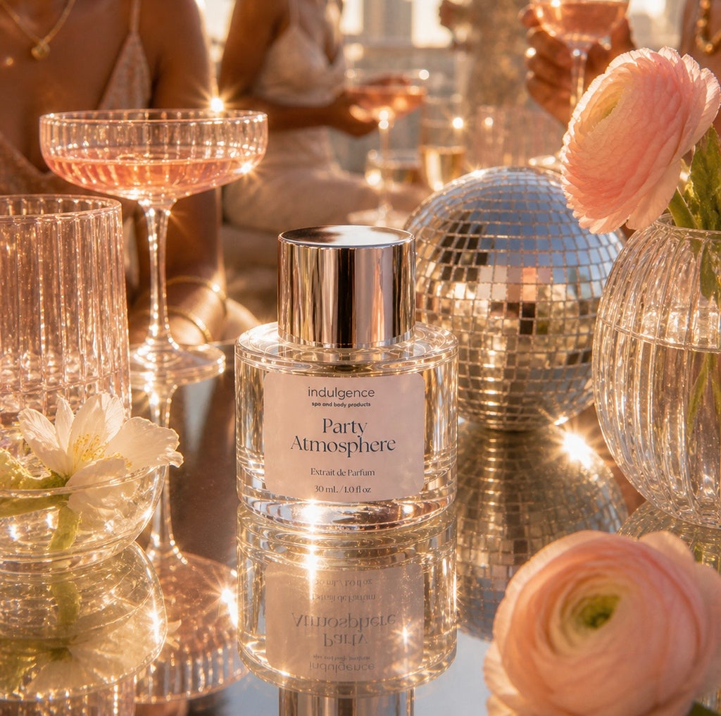 Perfume bottle labeled 'Party Atmosphere' on a reflective surface with disco balls and flowers in the background.