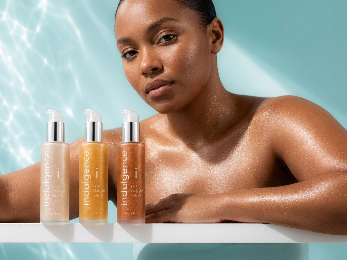 Woman with a towel around her neck next to Indulgence skincare bottles on a light blue background