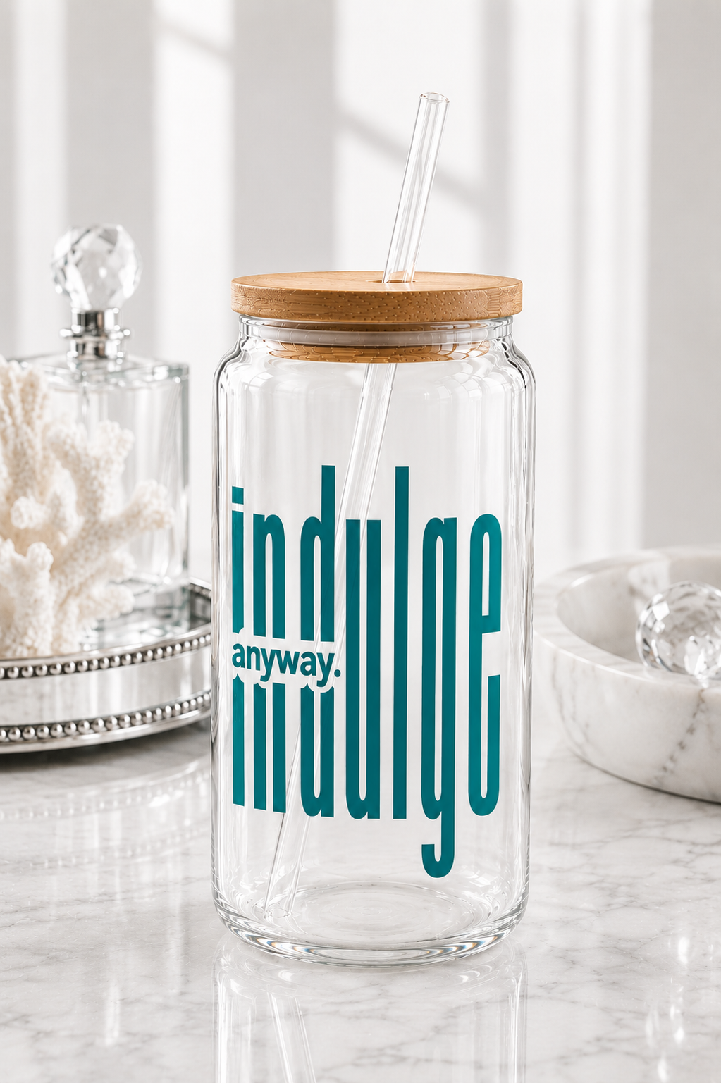 Glass jar with wooden lid and straw, featuring the text 'indulge anyway.' on a marble surface.